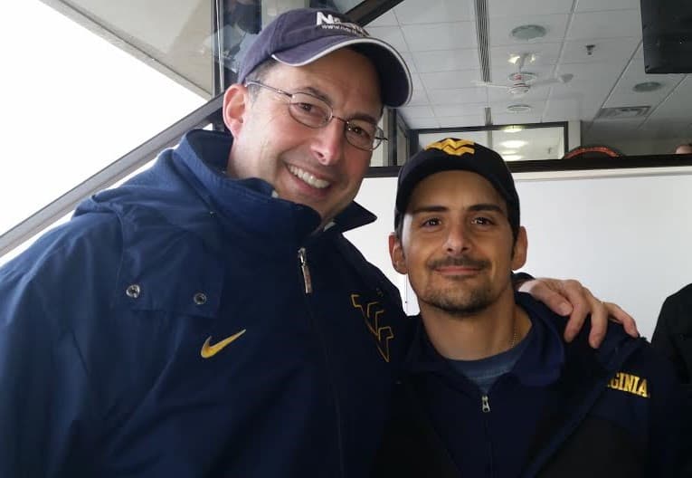 Tony Caridi in the broadcast booth, headset on, interviewing Brad Paisley during a West Virginia football broadcast.